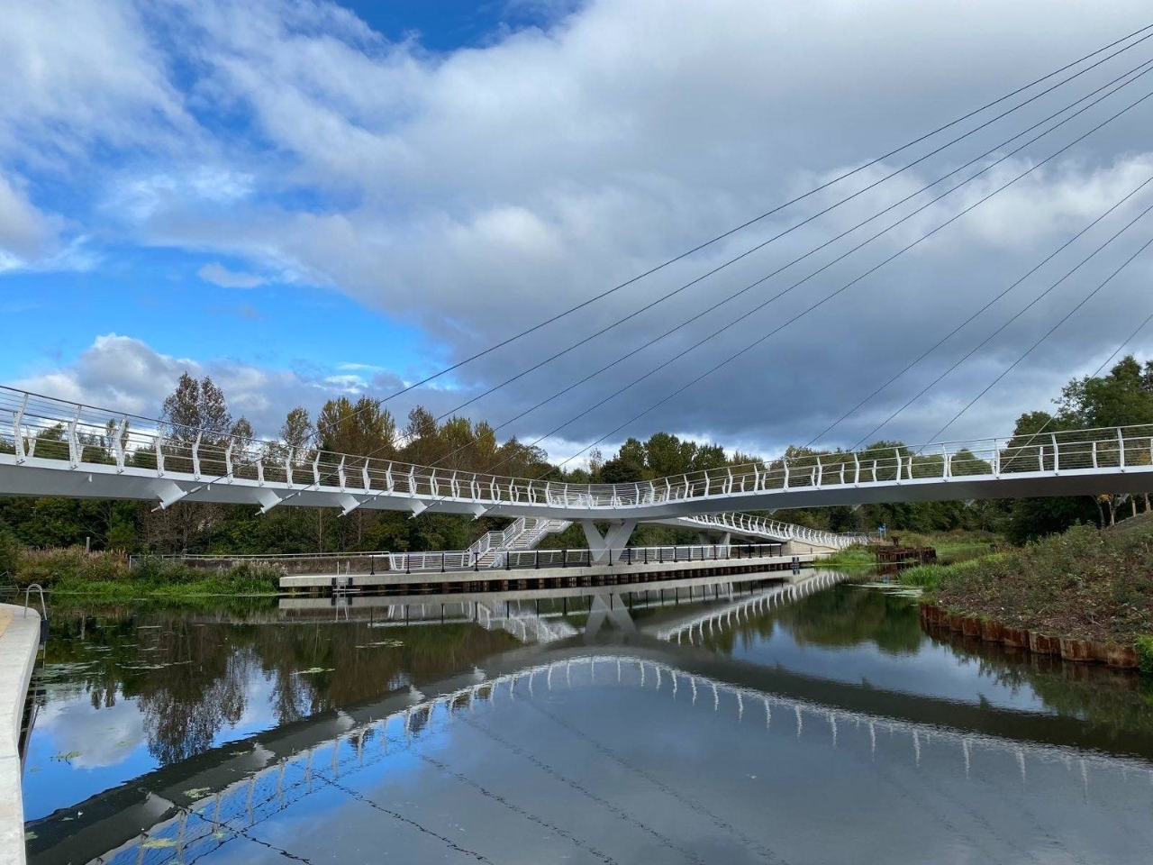 stockingfield bridge, a curved white bridge over the forth and clyde canal in maryhill, glasgow, with blue sky and clouds above, reflected in the water